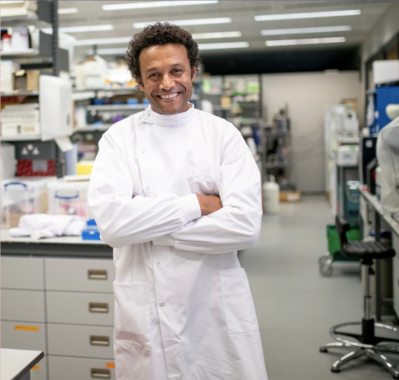 Medical professional standing and smiling with arms crossed in a lab.