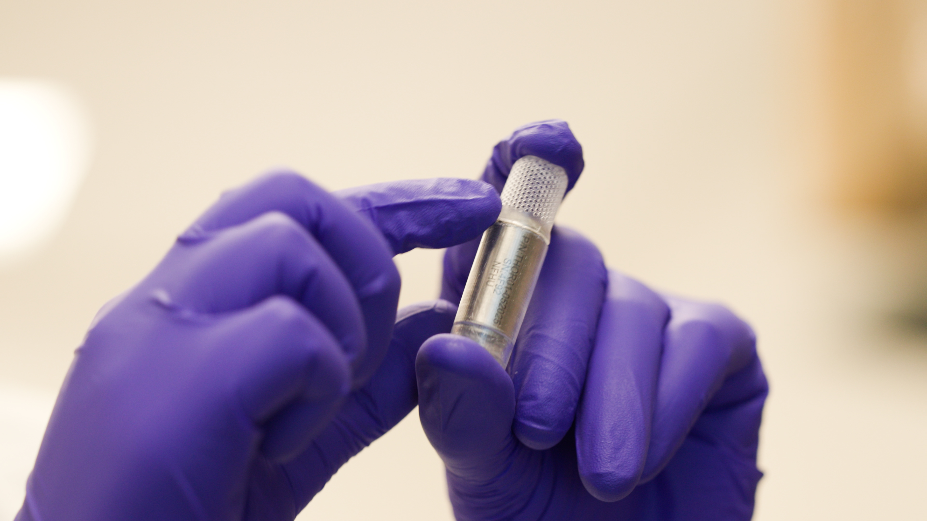 Gloved hands hold a small vial