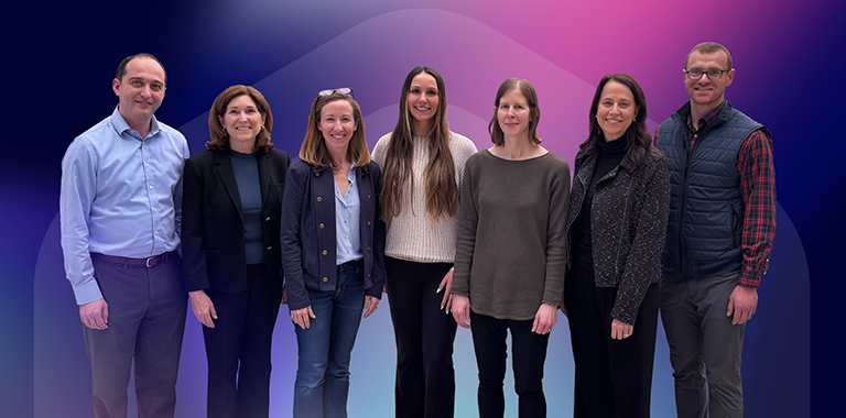 Draper lab group with ARPA-H PM Dr. Arnold in front of an agency branded pink and navy blue hexagon