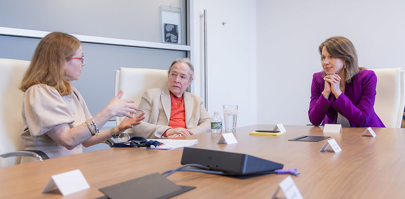 Three women sit around a table in discussion with one another.