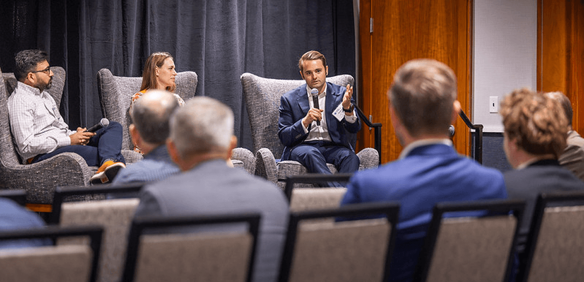 Three panelists answer questions from a room of seated attendees.