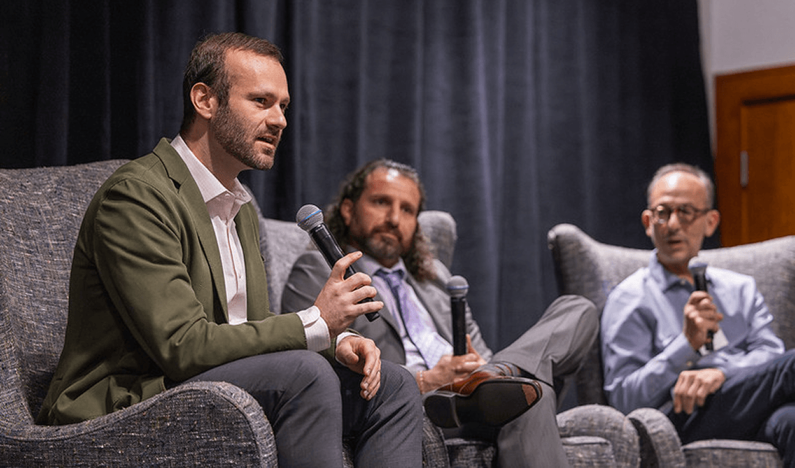 A man seated on a panel speaks into a microphone.